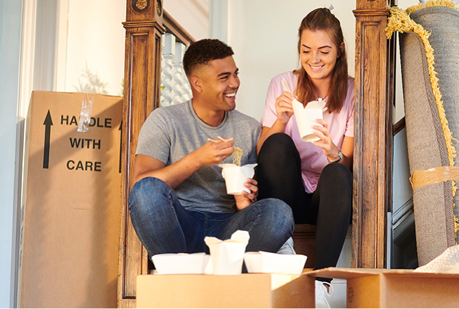 A couple eating together surrounded by moving boxes.