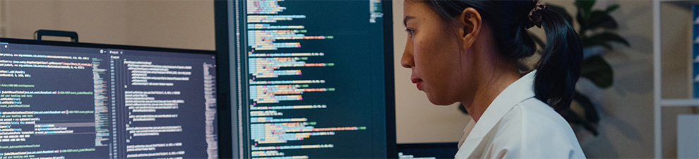 A person sitting at a desk that holds multiple computer monitors with computer code showing.