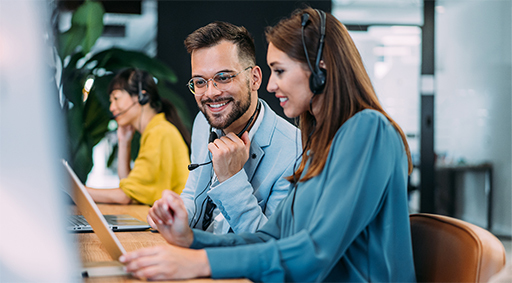 Two people with headsets looking at a computer screen.