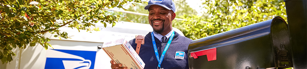 Letter carrier ready to deliver packages unloaded from the back of a USPS Next-Generation Delivery Vehicle.