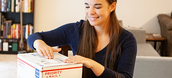 Una mujer joven etiqueta un paquete de Priority Mail International de USPS.