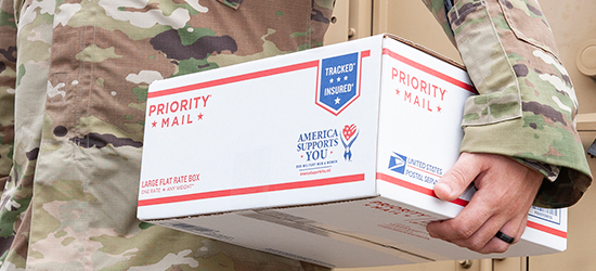 Un miembro del servicio militar sosteniendo una Caja Priority Mail Flat Rate Grande especial para a APO/FPO.