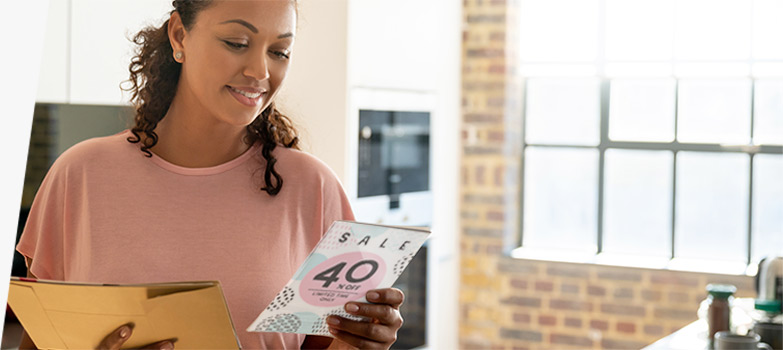 Una mujer leyendo una pieza publicitaria de correo directo que promociona una oferta.