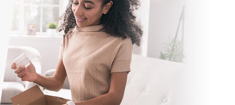 Young woman removes sample jar of cream from a marketing mail parcel.