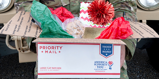 Man in military uniform holding a box full of holiday gifts.