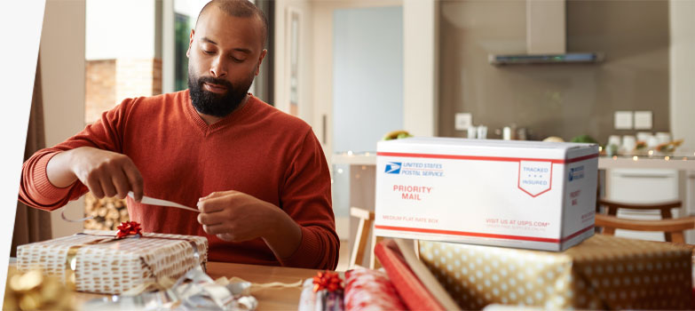 A person preparing a holiday package to ship in a Priority Mail box.