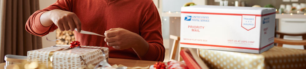 A person preparing a holiday package to ship in a Priority Mail box.