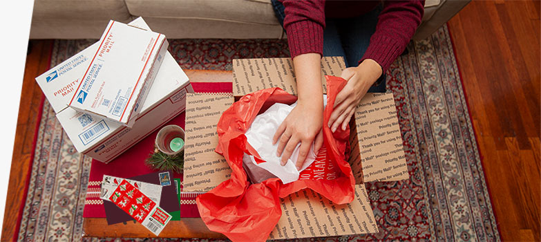 Young woman preparing holiday gifts and Priority Mail boxes to ship for December 25 delivery.