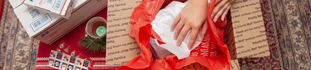 Mujer joven preparando regalos de días festivos y cajas de Priority Mail para enviar para la entrega del 25 de diciembre.