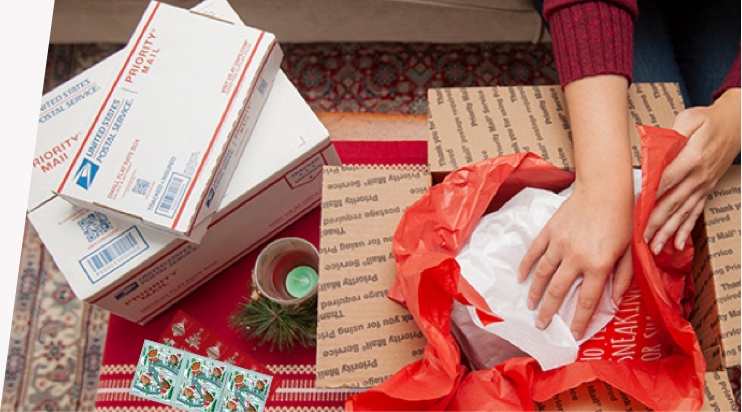 年轻女子准备假日礼物和 Priority Mail 包装盒寄送，以能够 12 月 25 日前投递。