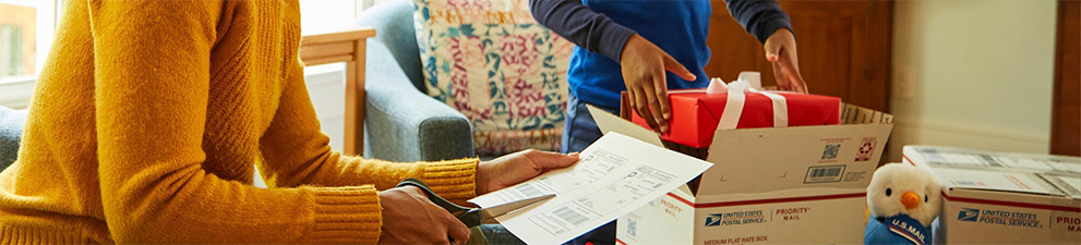 Two people preparing holiday gifts and Priority Mail boxes to ship for December 25 delivery.