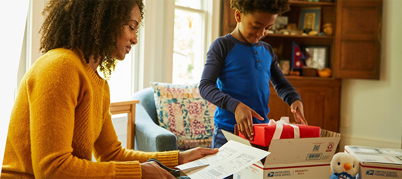 Two people preparing holiday gifts and Priority Mail boxes to ship for December 25 delivery.