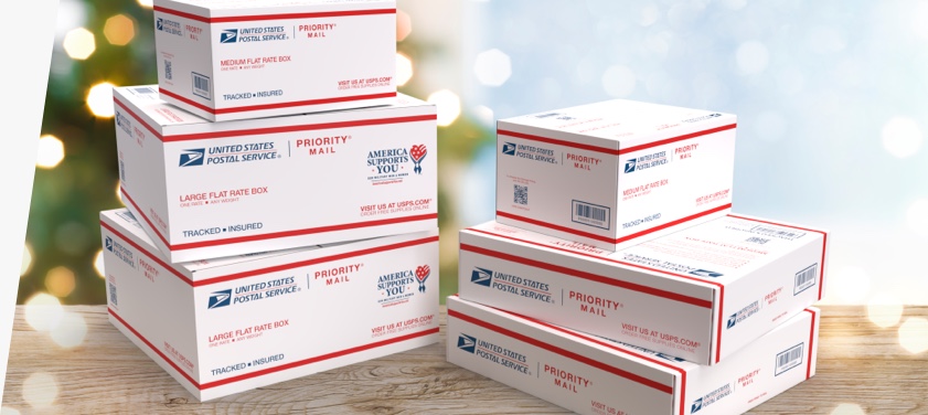 A variety of Priority Mail® boxes, including Priority Mail® APO/FPO Large Flat Rate Boxes, stacked on a table.