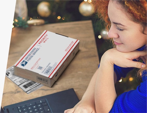 Mujer con computadora portátil con caja de Priority Mail y etiqueta de envío impresa en la mesa junto a ella.