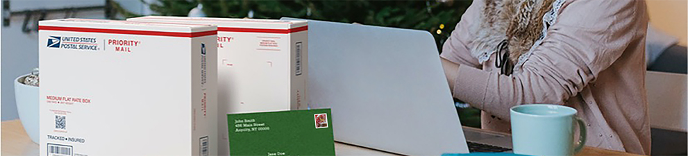 一位女士在笔记本电脑前准备运送 Priority Mail 包装盒和一张带有节日主题邮票的卡片。