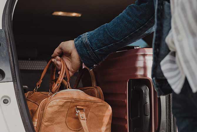 A brown traveling bag being loading into a car.