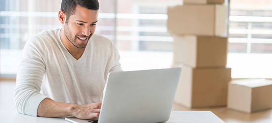 Image of a man sitting in a chair using a laptop with packing boxes in the background.
