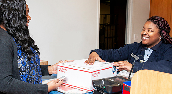 Una persona entrega un paquete de Priority Mail a un empleado de ventas minoristas en el mostrador de una Oficina Postal.