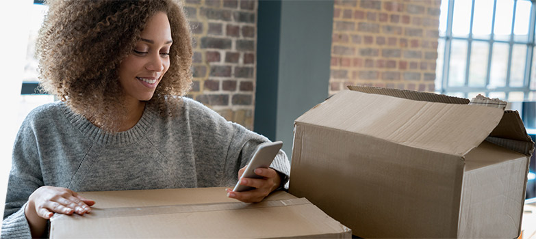 一名妇女一边使用她的智能手机一边准备包装盒。