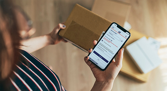 Person with a sealed package, holding a smartphone showing a Click-N-Ship screen and the option to 'Print later at Post Office.'