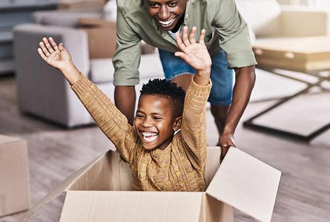 Image of an excited young man riding in a box with his dad propelling him.