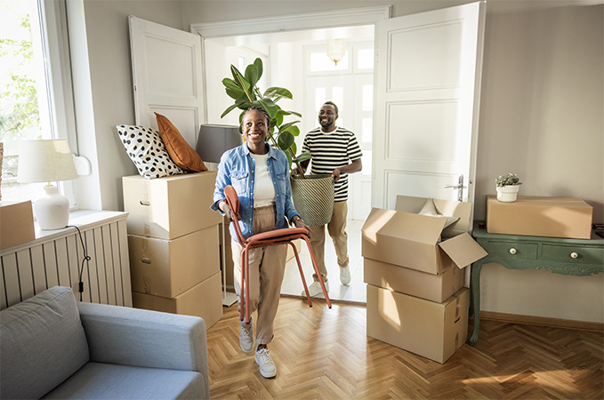 Two people carrying boxes full of items through a doorway.