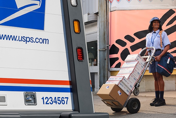 Letter carrier ready to deliver packages unloaded from the back of a USPS Next-Generation Delivery Vehicle.