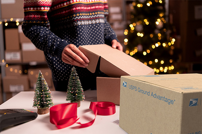 USPS Ground Advantage. A person packing a shipping box with holiday decorations behind them.