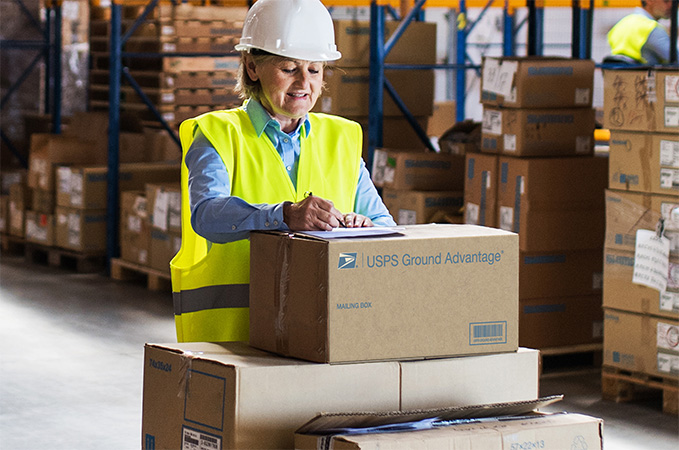 USPS Ground Advantage。A person in a high visibility vest surrounded by shipping boxes.