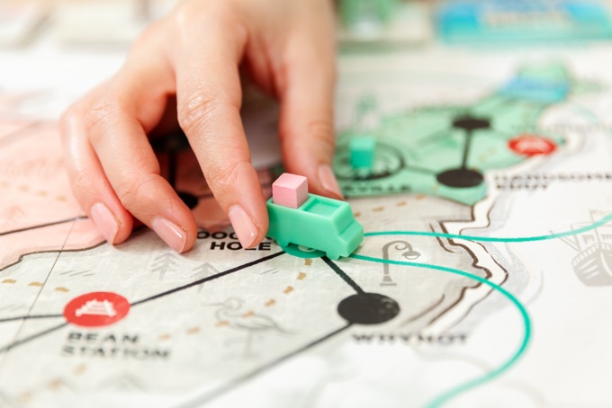 A hand moving a piece of the board game 'USPS The Great American Mail Race'.