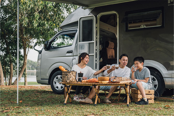 A family sitting outside an RV amongst trees.