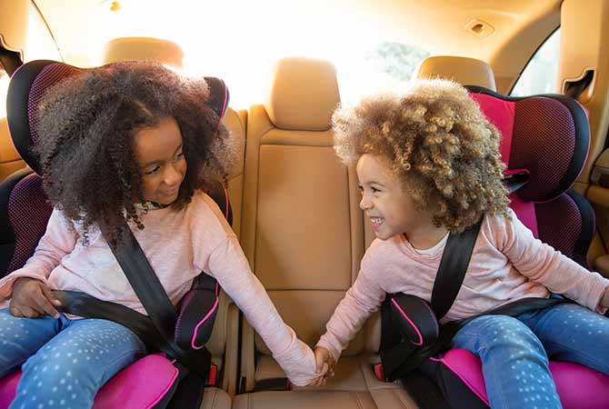 Siblings holding hands while traveling safely in a car.