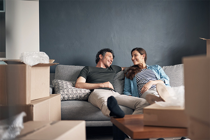 Two people sitting on a couch surrounded by moving boxes.