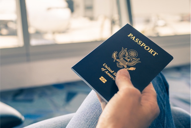 Una persona sosteniendo un pasaporte sentada en un aeropuerto.