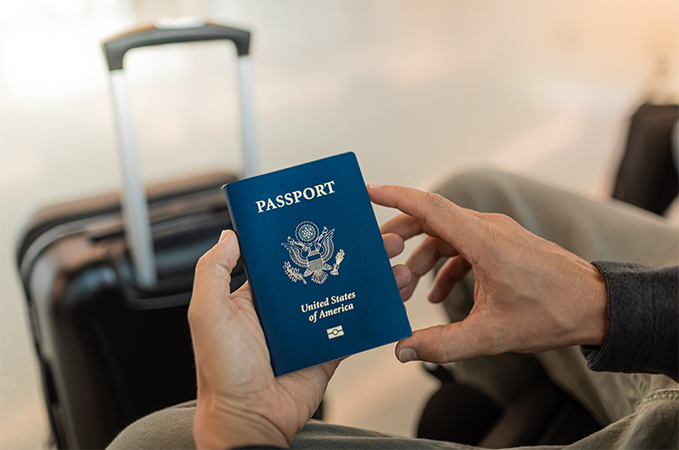 A person holding up a passport with luggage in the background.