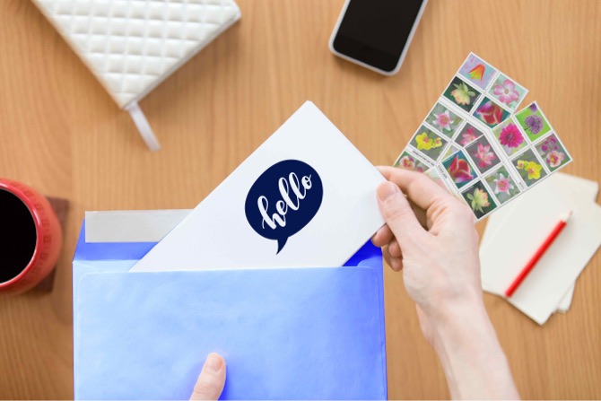 Person preparing to put a 'hello' card into an envelope, with Forever stamps for sending.