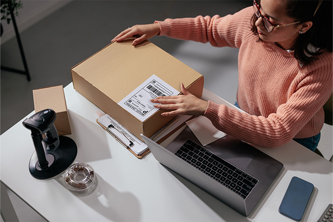 A woman at a desk places a Click-N-Ship label on an outgoing package.