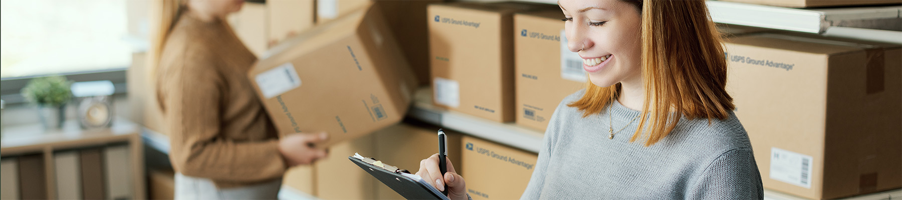 A person standing in front of a shelf of USPS Ground Advantage packages in a delivery center.