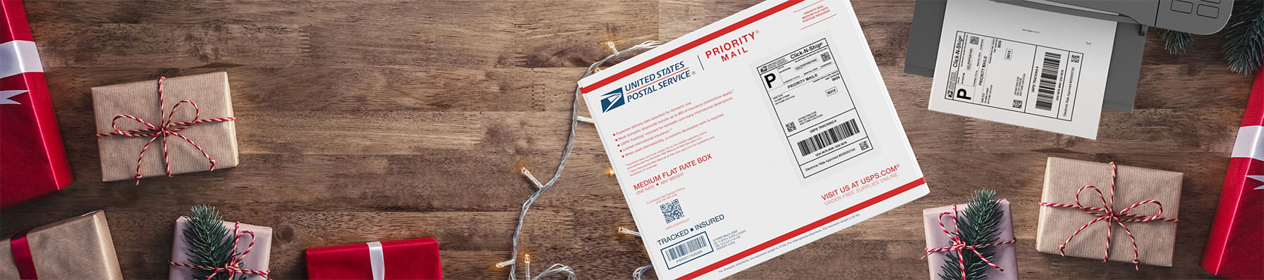 Priority Mail box on a table with wrapped gifts and a Click-N-Ship label in a printer tray.