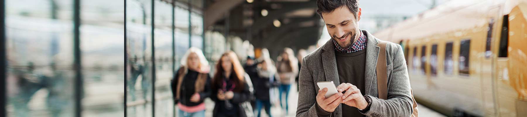 Person smiling and checking smartphone at a train station.